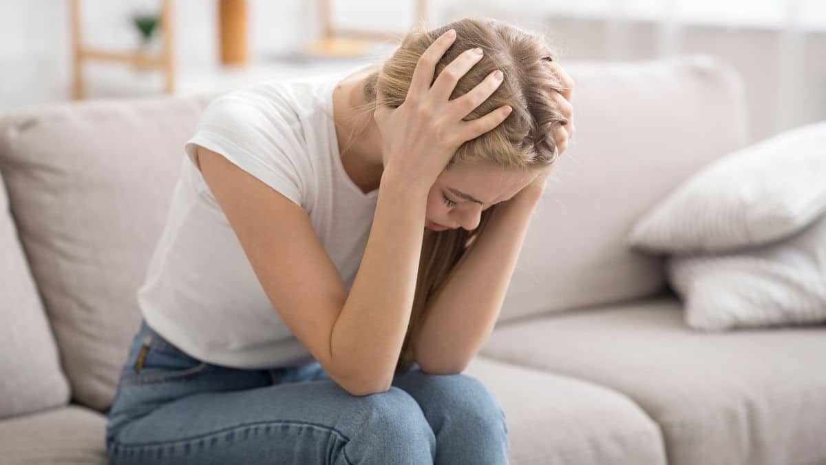 Woman upset looking down, sitting on the couch hand at her head