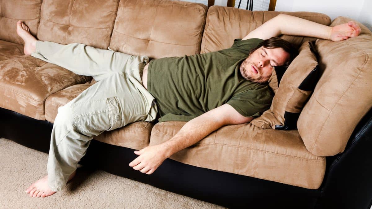 Man laying on a brown couch looking lazy.