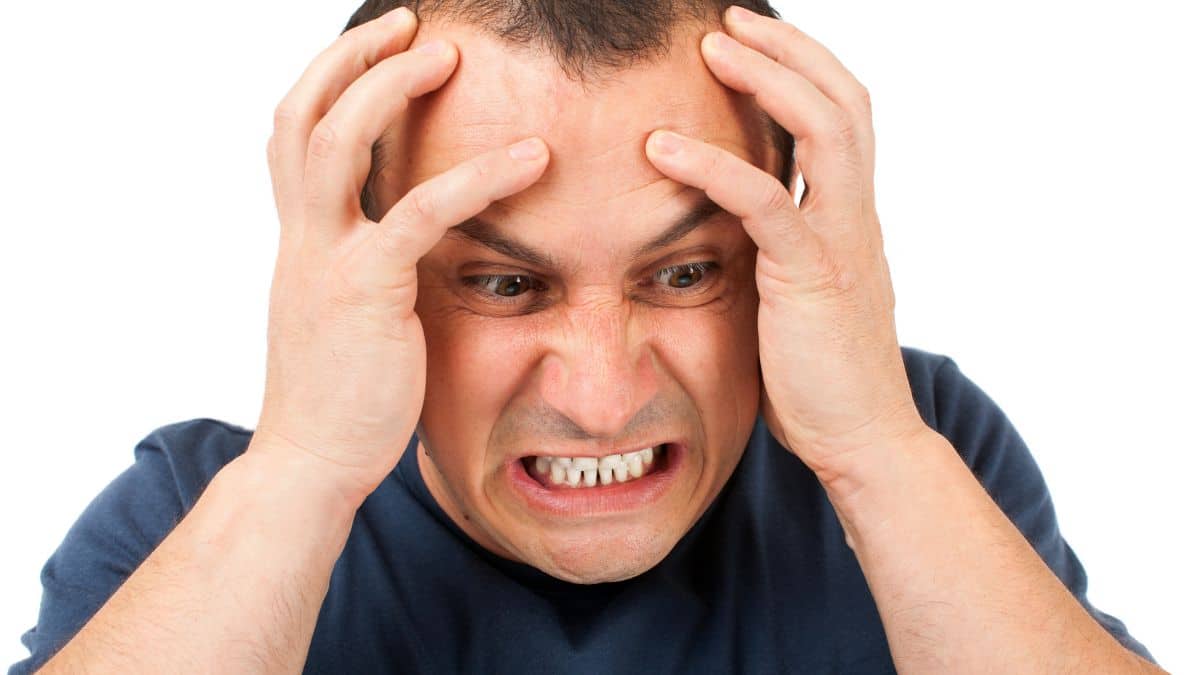 Man wearing a blue shirt looking frustrated and holding his face in anger