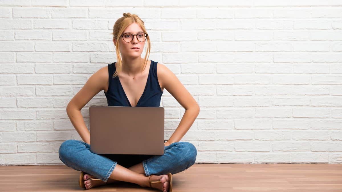 woman sitting on the floor looking uncertain with her laptop