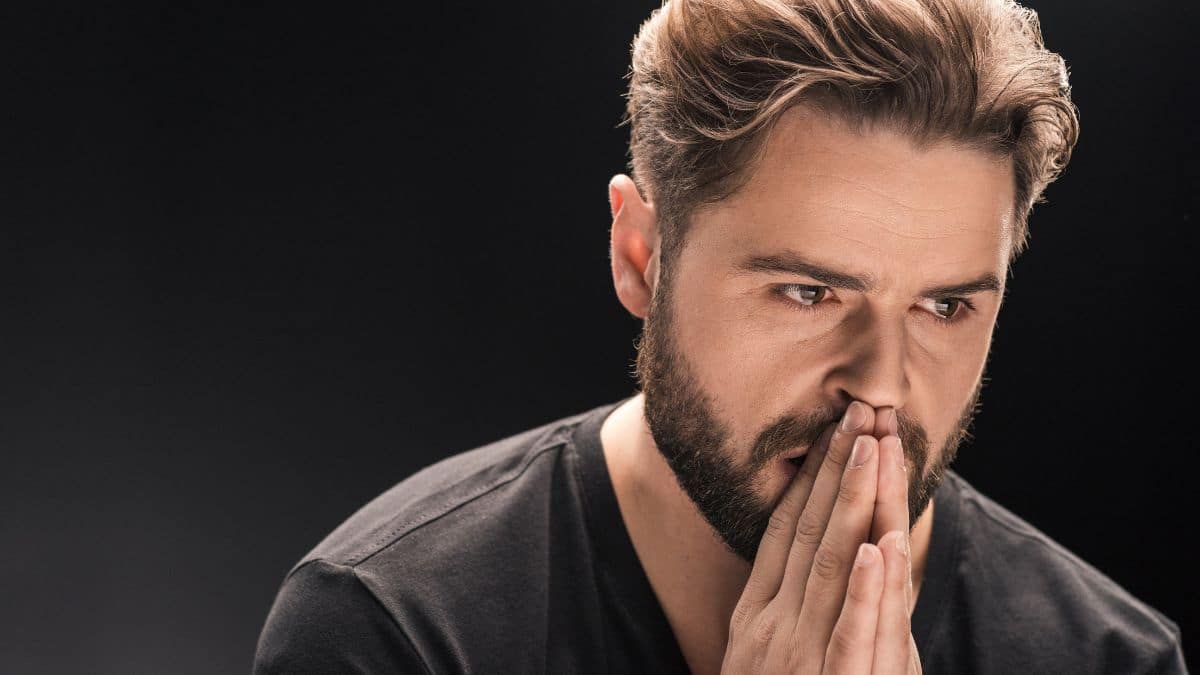 crying man with hands in prayer by his mouth