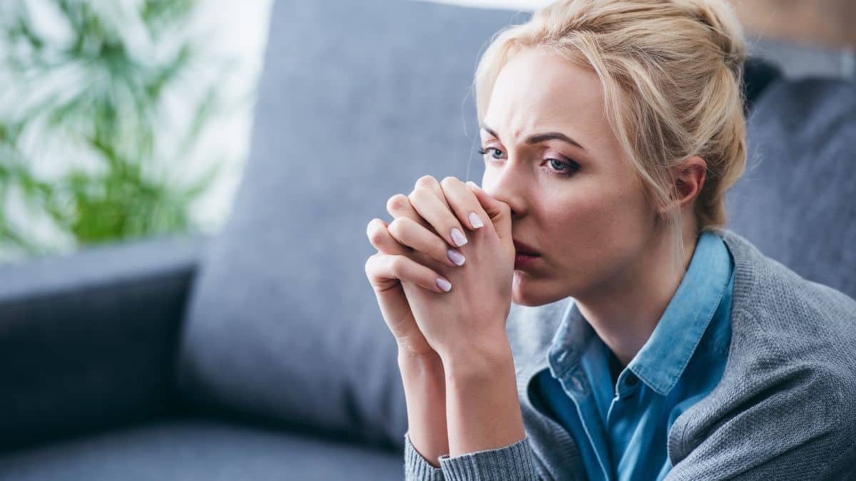 upset woman sitting with her hands clasped at her mouth